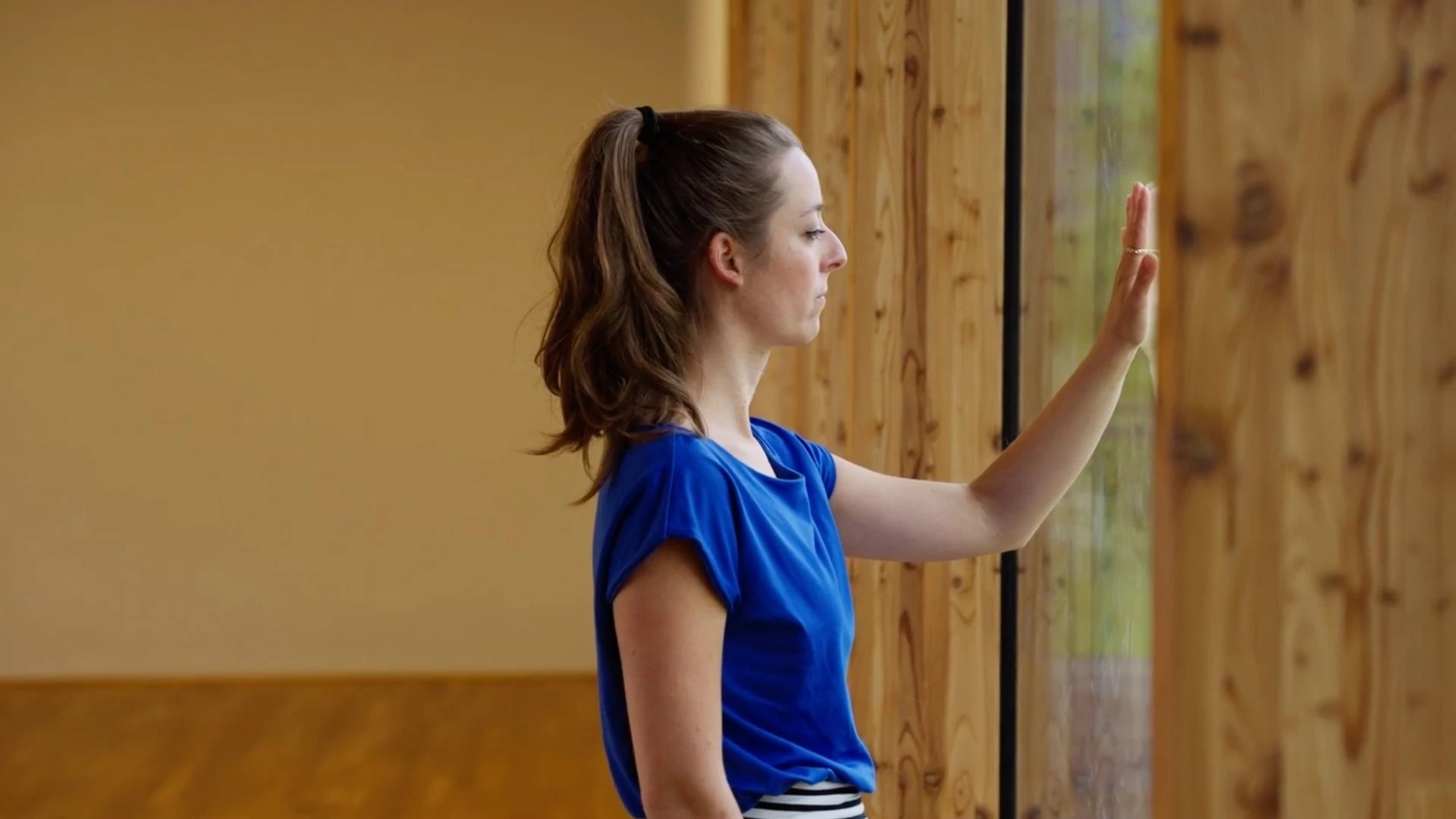 Still aus Traumasensibles Embodiment und Stimmtransformation: eine Frau legt ihre Hand an ein Fenster in einem holzvertäfelten Raum